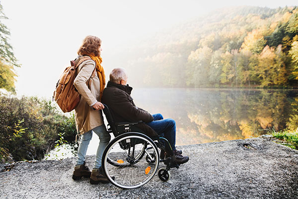Young woman pushing older man in wheelchair around a pond